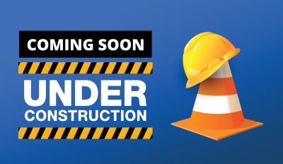 sign saying coming soon under construction with a caution cone and a hard hat sitting on top 